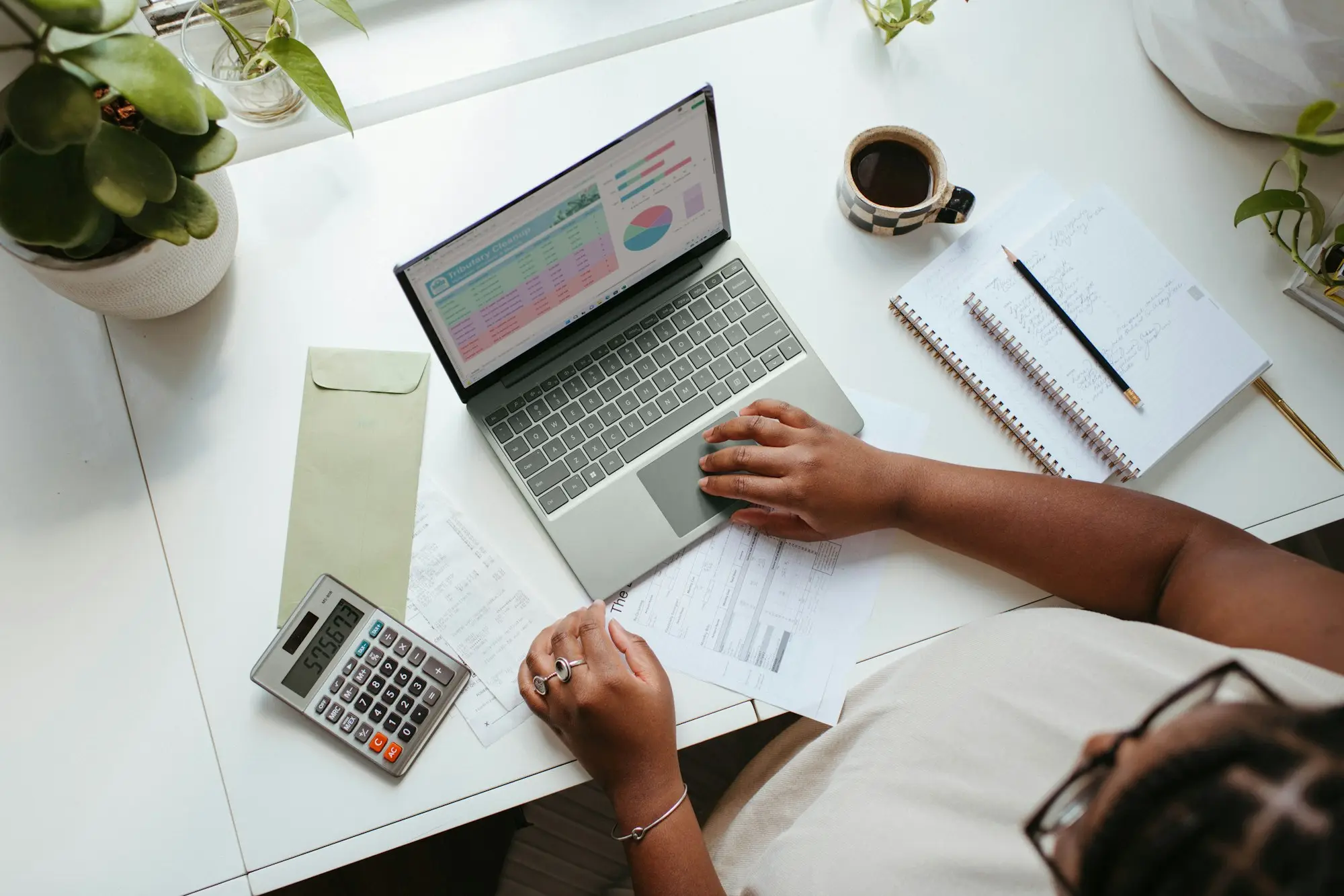 Overhead view of a business owner working through figures with a laptop, calculator and notes