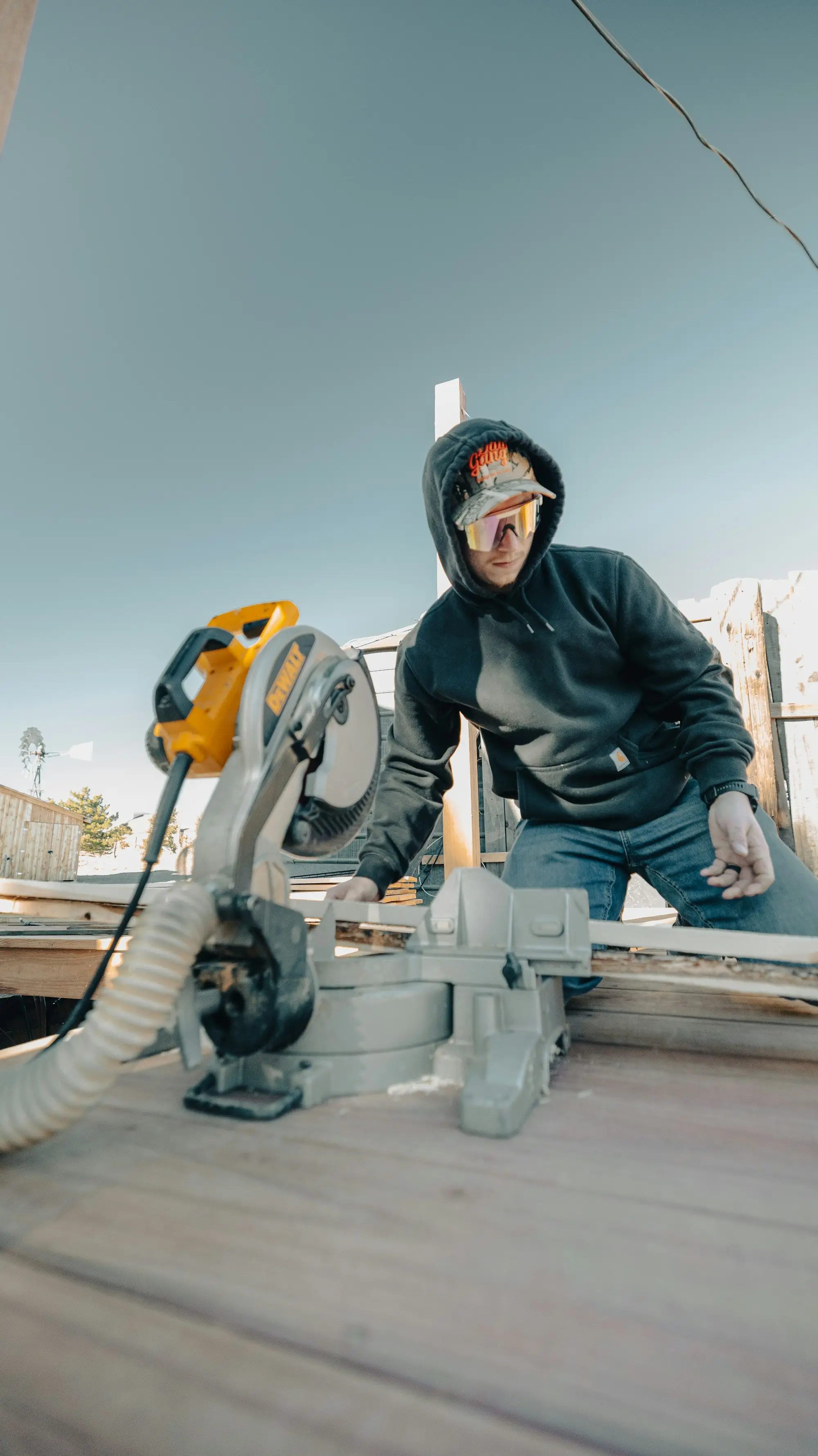 Carpenter in a hoodie cutting timber with a mitre saw on a new outdoor deck