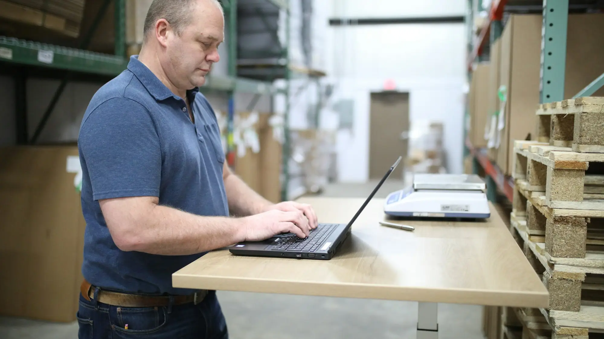 Online store owner typing on a laptop at a standing desk in his stockroom