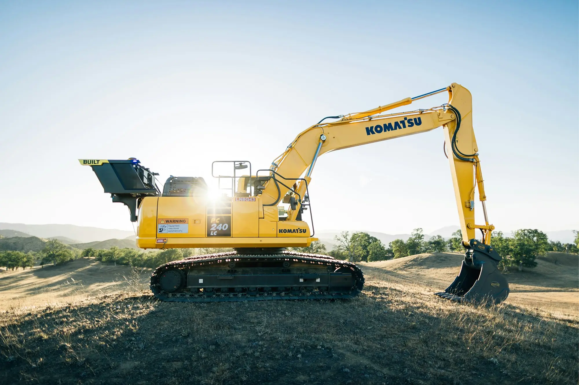 Excavator on a dirt earthworks site with the sun low behind the boom