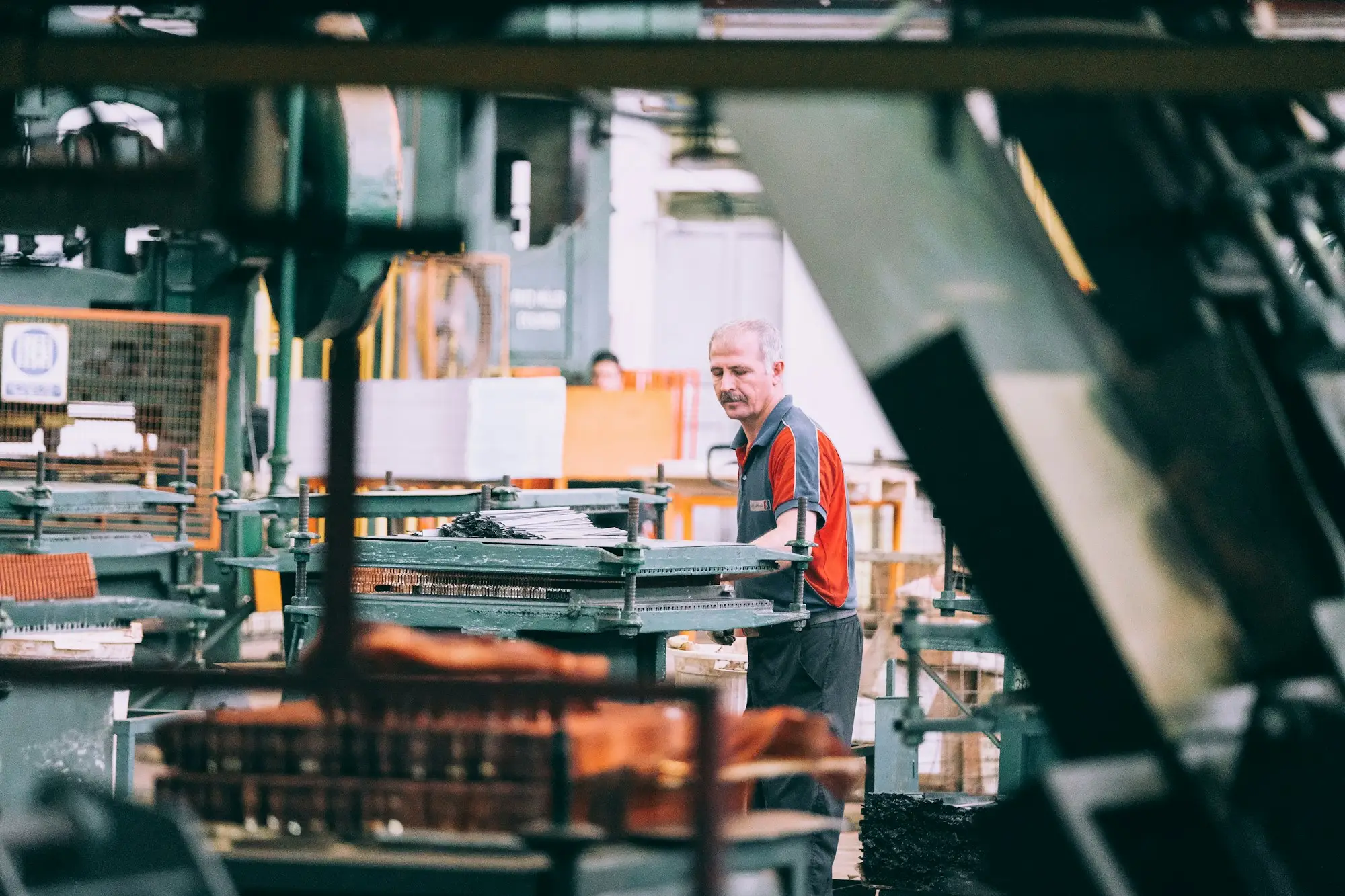 Operator in a work shirt running industrial machinery on a busy factory floor