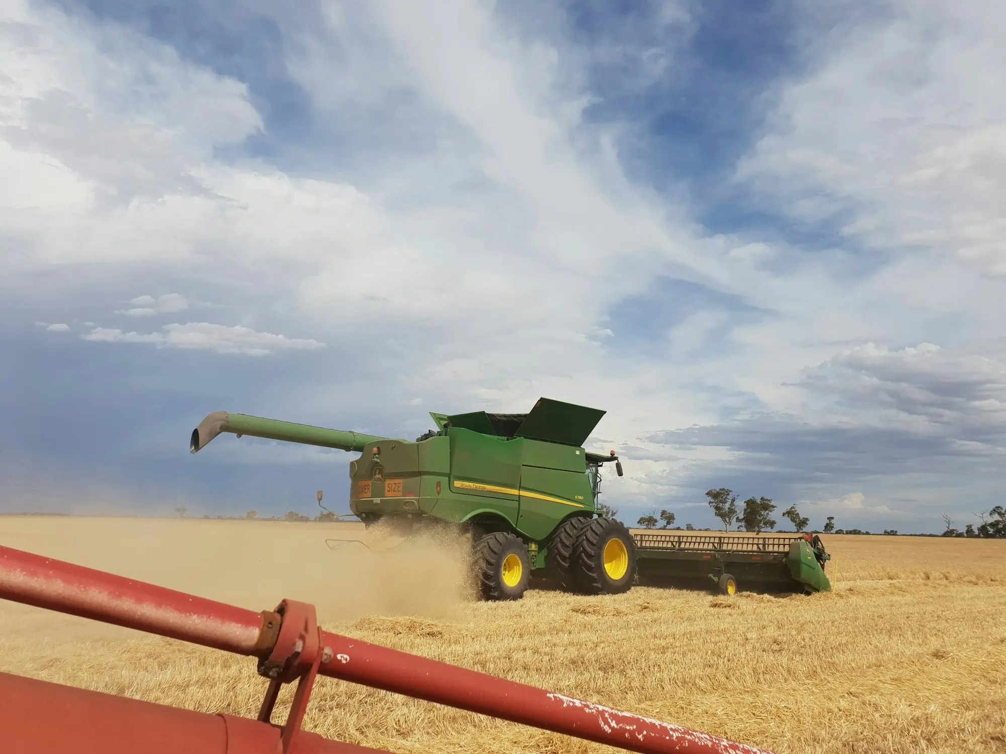 Green combine harvester working through a golden wheat crop under a big sky