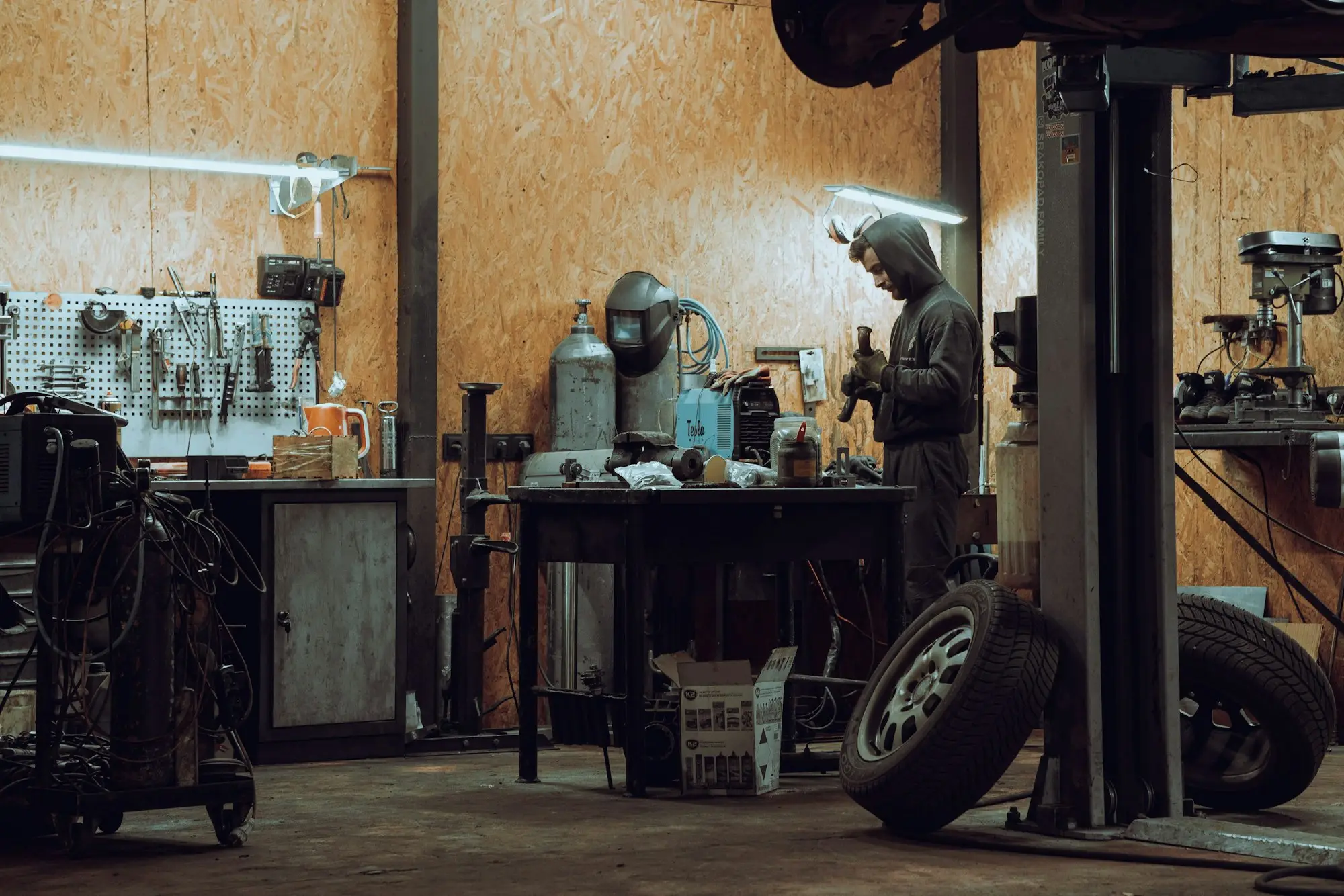 Mechanic working at a bench in a well-equipped vehicle workshop with a hoist