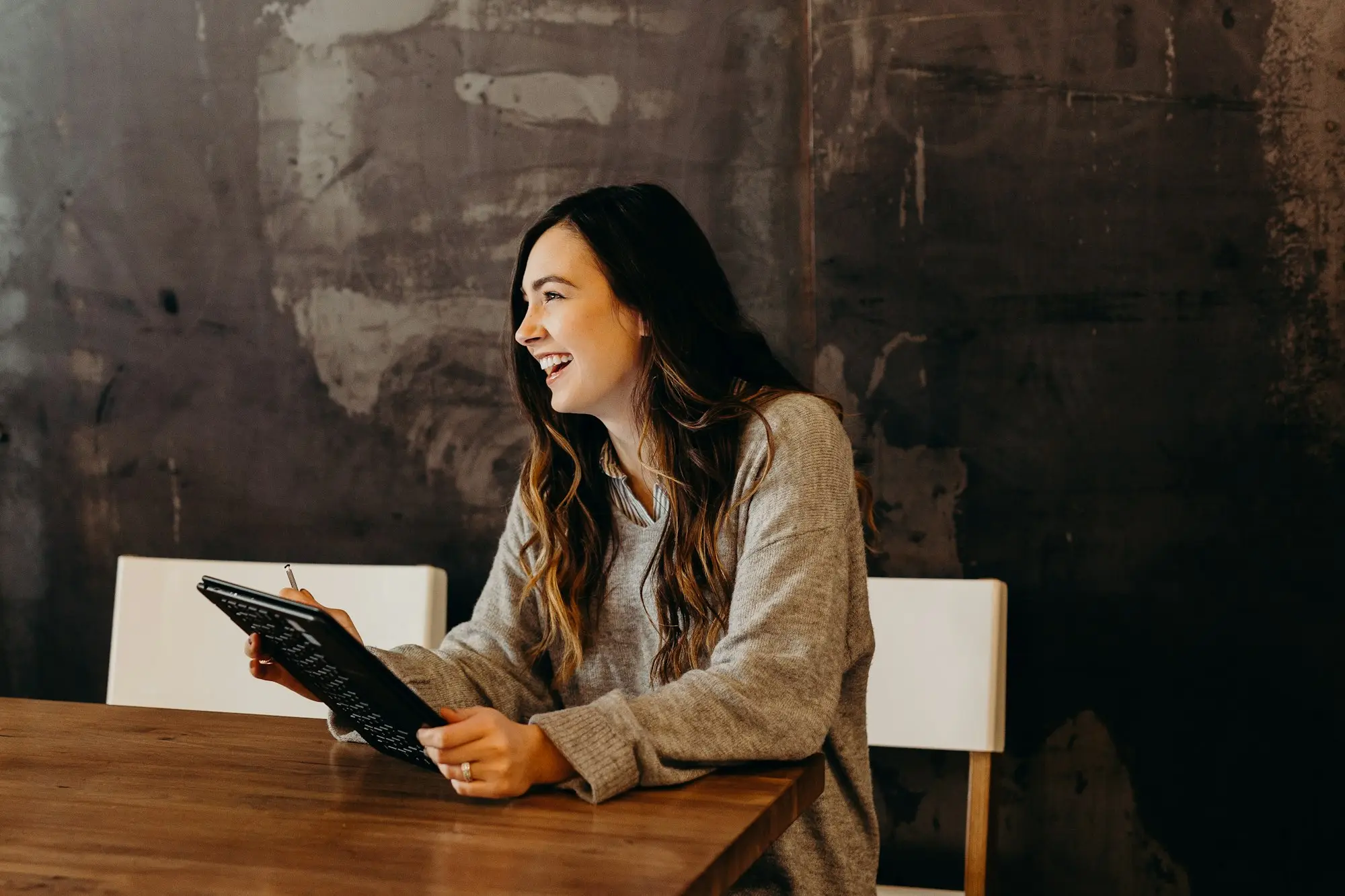 Business owner laughing while reviewing figures on a tablet at a timber table